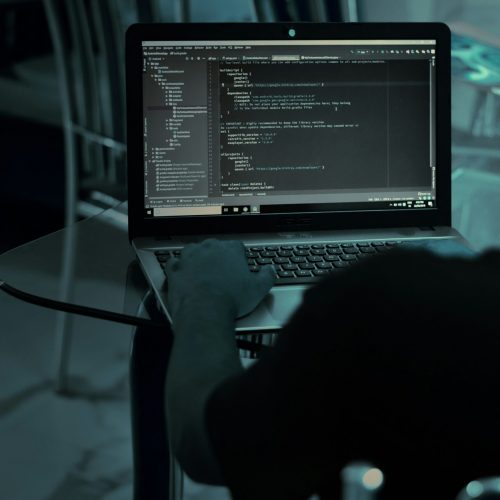 Man in a dark room coding at his laptop